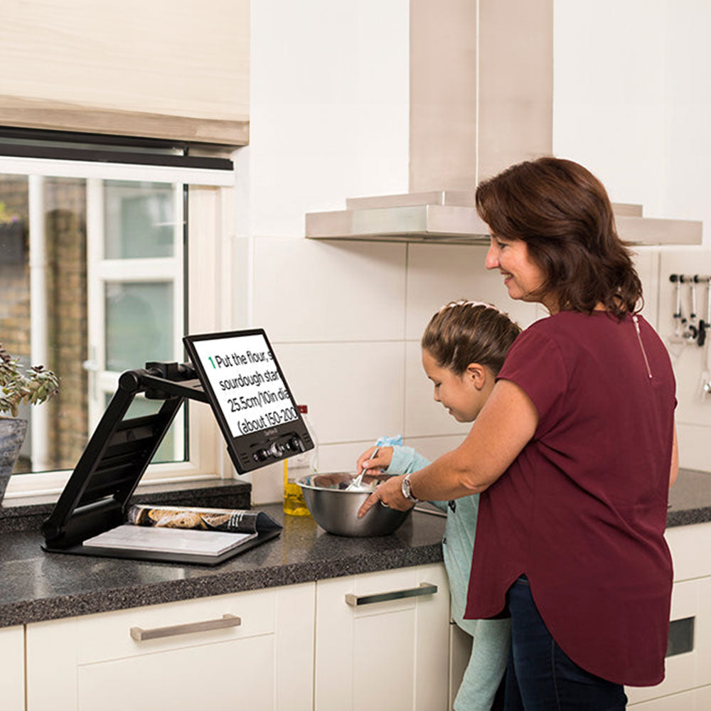 Woman baking with child while using ClearView GO to magnify recipe