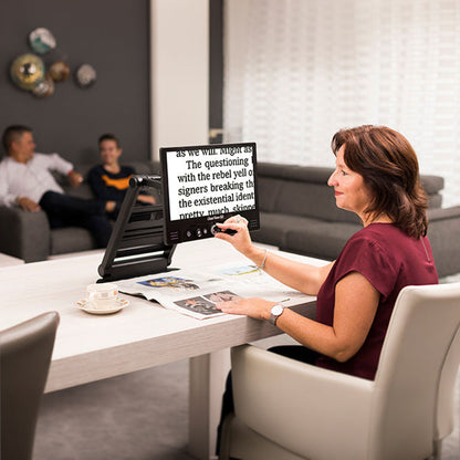 Woman sitting at table using ClearView GO to magnify magazine